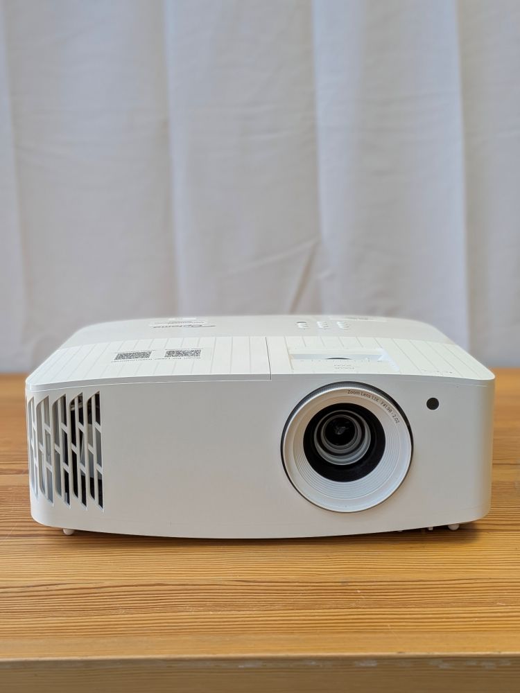 Compact white Optoma 4K projector rental unit with ventilation grilles and large zoom lens on a wood table