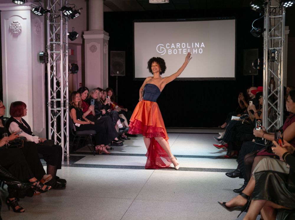 Full runway stage with overhead lighting trusses, floor spotlights, and AV projection screen at an indoor fashion event
