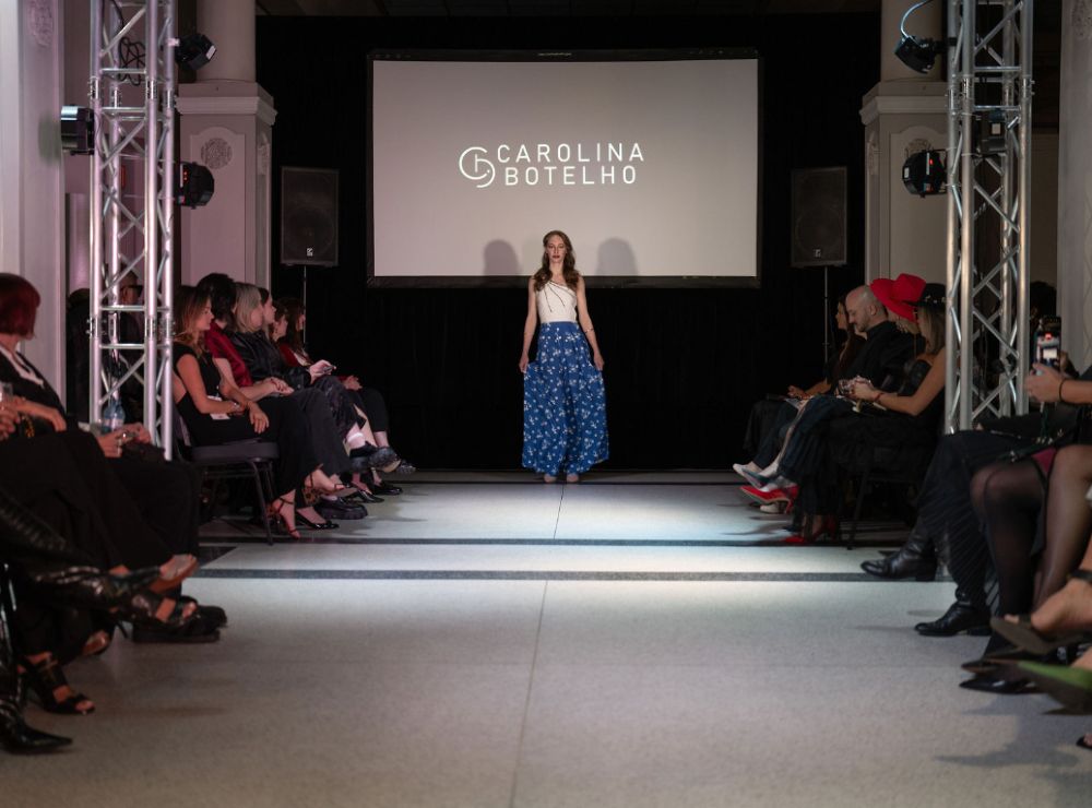 Wide runway stage with symmetrical lighting trusses, rear projection screen, and audience seating on both sides
