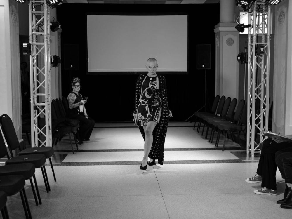 Black and white photo of a lit fashion show runway with truss structures and stage lighting equipment visible