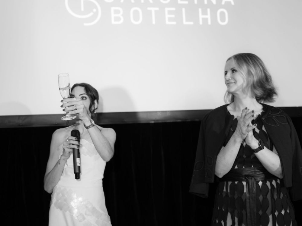 Large rear projection screen displaying the Carolina Botelho branding as a backdrop on the event stage