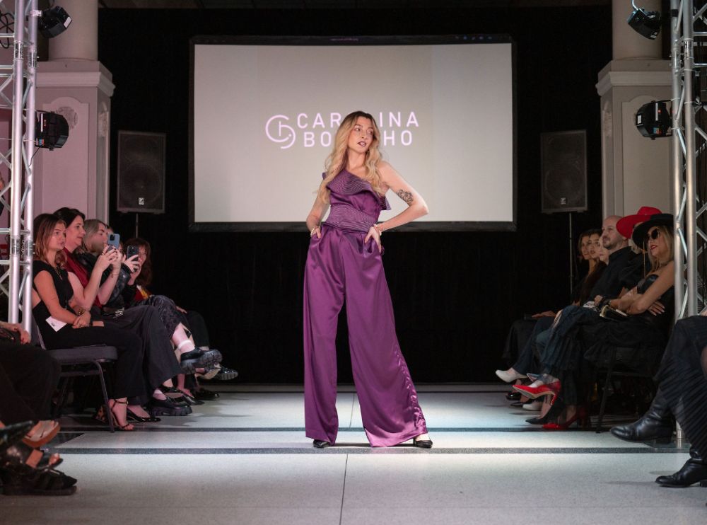 Model walking the runway in a purple satin wide-leg jumpsuit at the Carolina Botelho fashion show