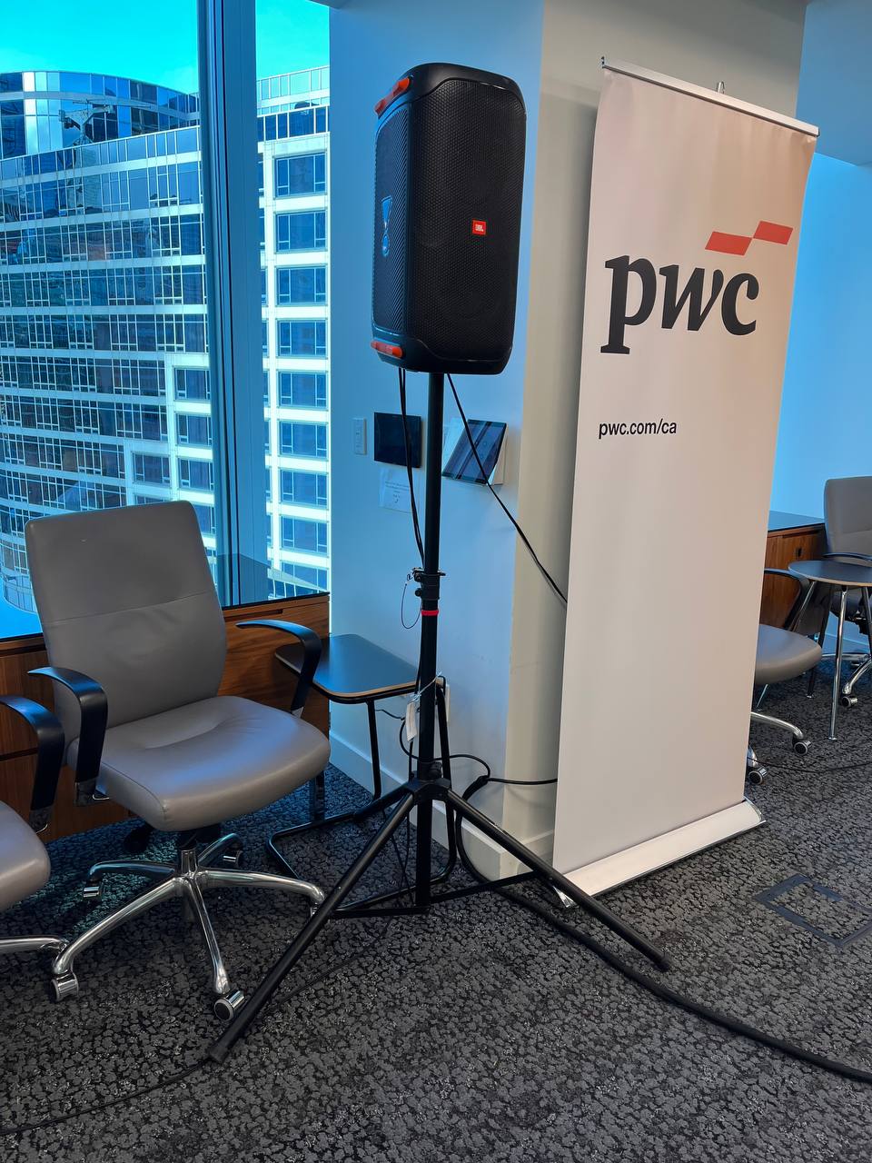 Corporate event audio setup featuring a portable speaker on a stand and presentation lectern in front of a PwC banner