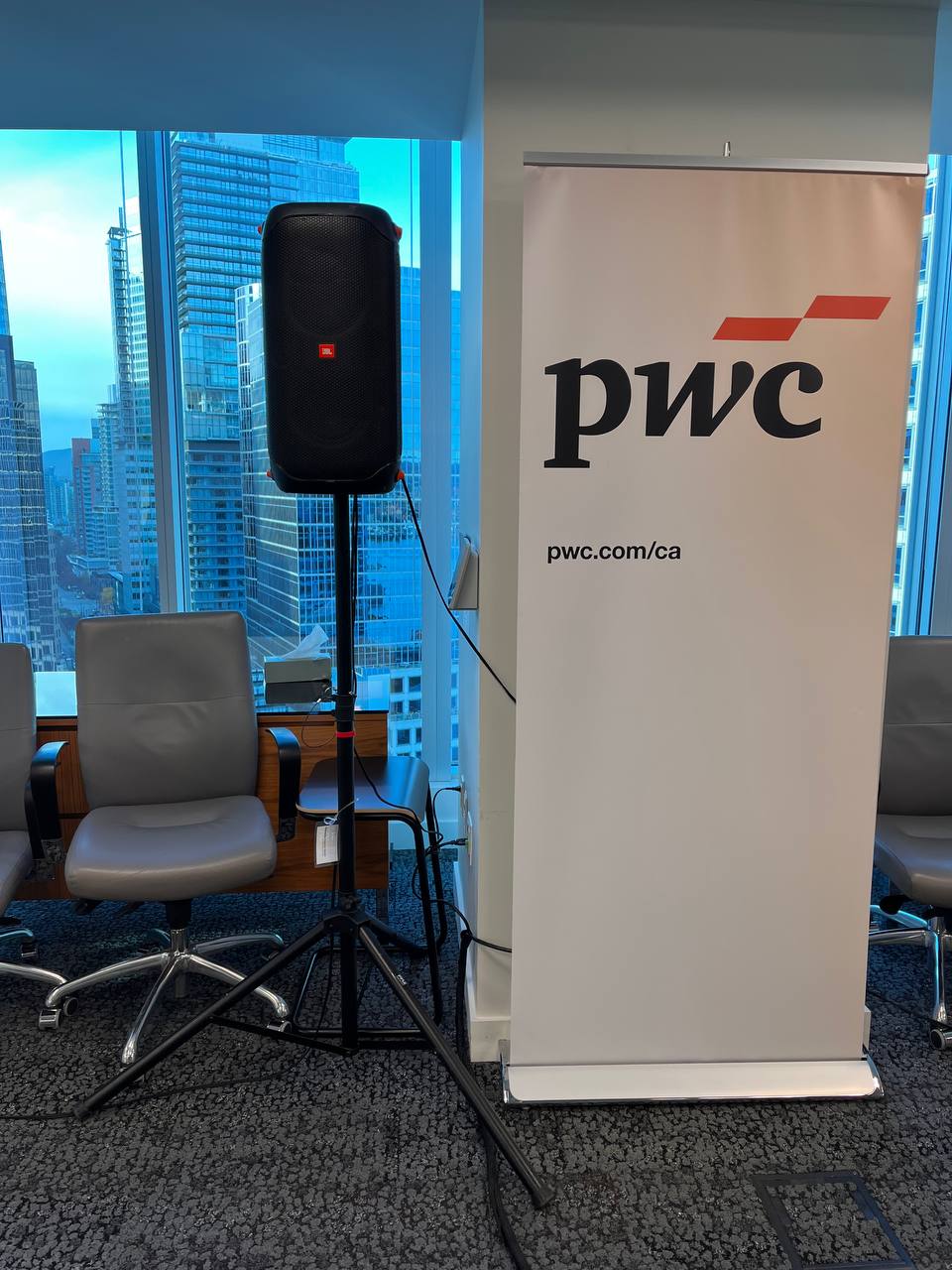JBL speaker rental mounted on a tripod stand next to a PwC branded banner in a Vancouver high-rise event space