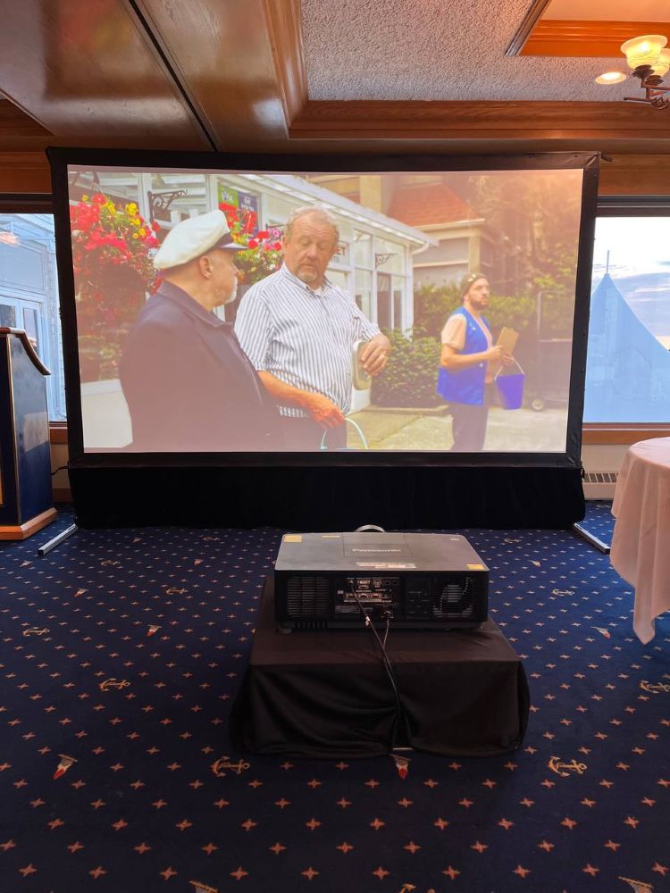 Professional projector and screen rental setup in a Vancouver banquet hall with video playing on a wide fast-fold display