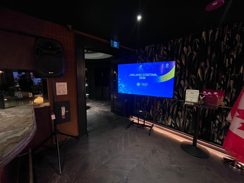 Wide-angle view of a large TV rental showing CBC Olympic Games coverage at a Vancouver bar event with Canadian decor