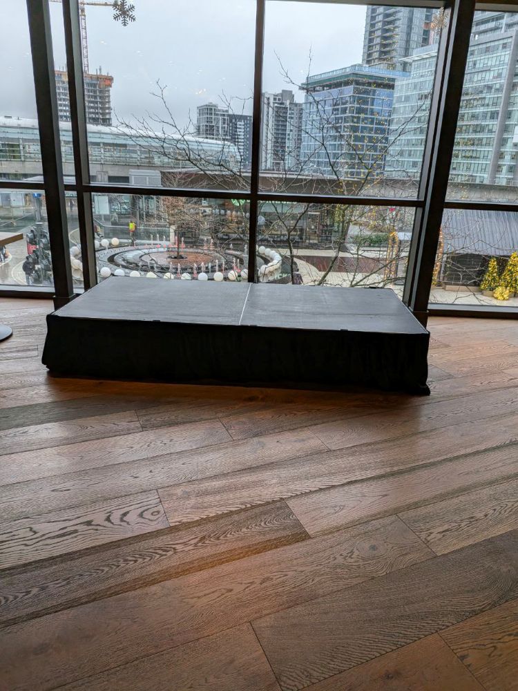 Portable stage riser rental set up on a wood floor in a modern Vancouver event space with a winter cityscape backdrop