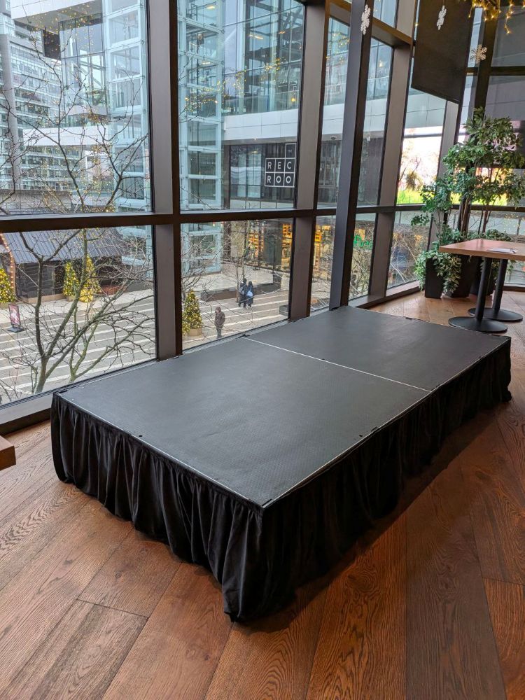 Portable stage riser rental for a corporate presentation at a Vancouver indoor venue with large windows and holiday decorations