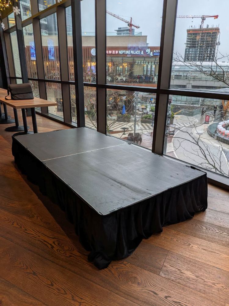 Low-profile stage platform rental with black skirting in a Brentwood Vancouver event space with panoramic winter city views