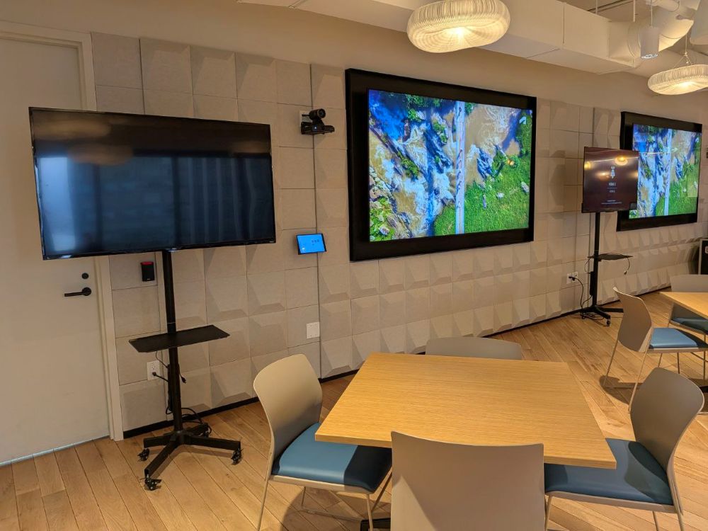 Multiple flat screen TV rentals on rolling stands set up alongside wall-mounted displays in a corporate event space with round pendant lighting