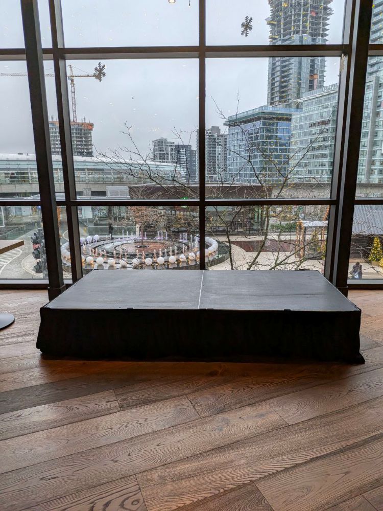 Low-profile stage platform rental with black skirting in a Brentwood Vancouver event space with panoramic winter city views