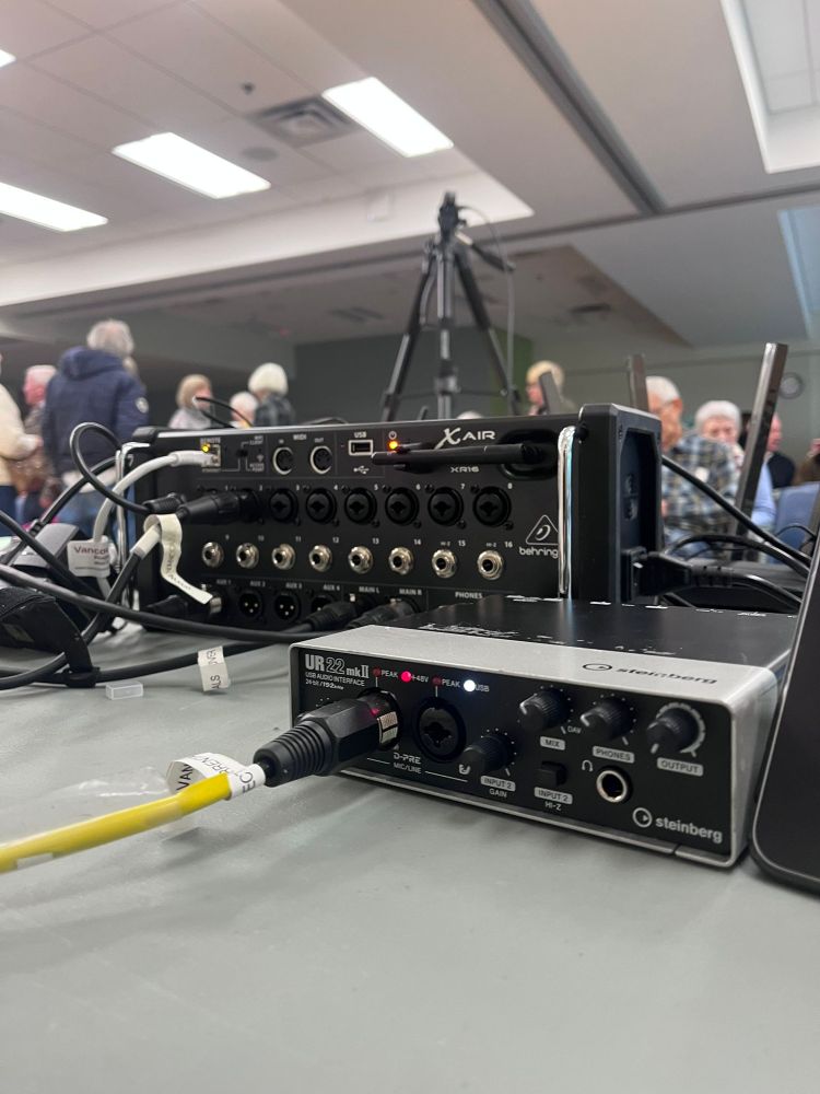 Hybrid-Livestreaming-setup-in-Delbrook-Community-Centre Seniors conference at Delbrook Community Centre with a full audience facing a projected presentation screen and panel of speakers at the front