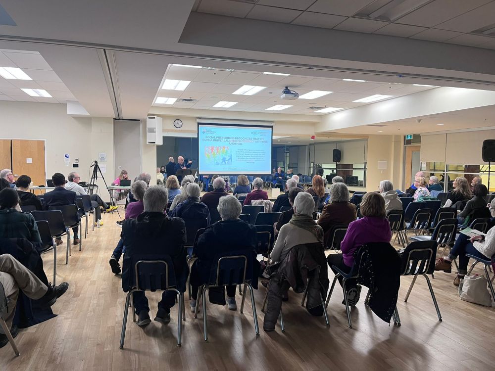AV rental setup at a North Vancouver community conference featuring a ceiling projector, large projection screen, camera tripod, and PA speaker for a hybrid event