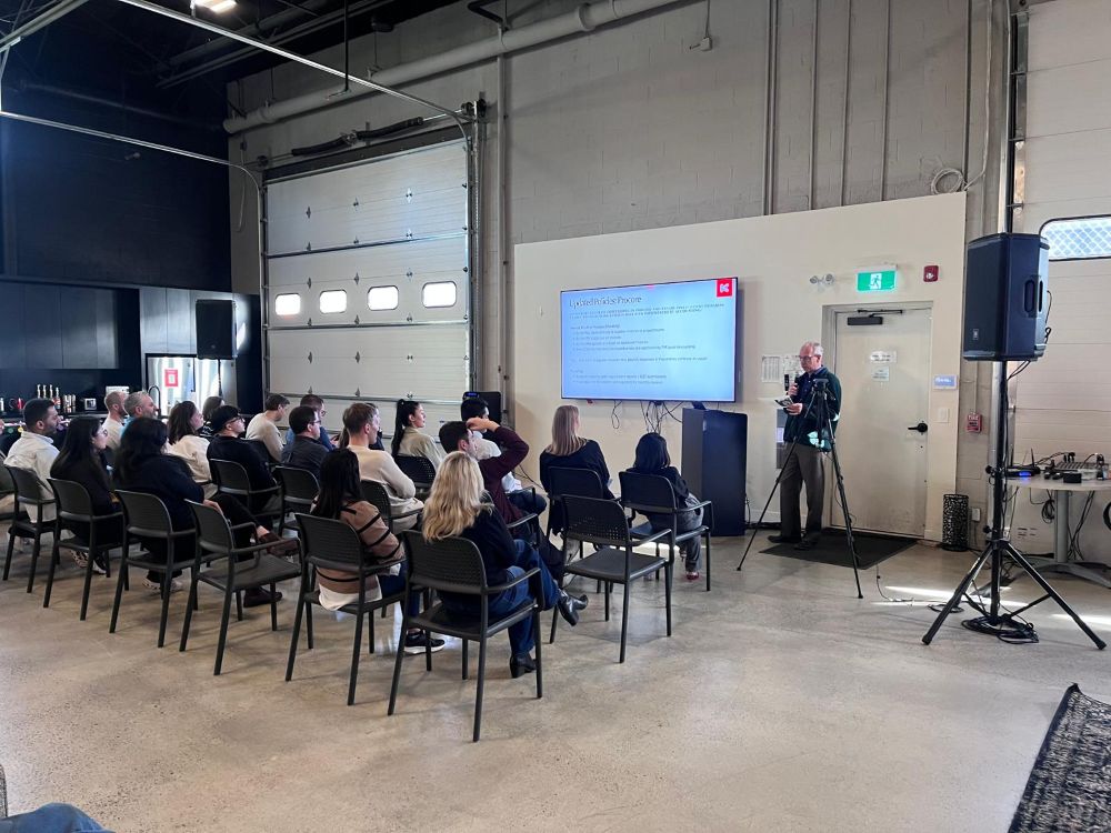 Small audience watching a corporate presentation with TV rental and PA speaker on a tripod stand in a Vancouver warehouse event space