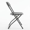 Side view of a black folding chair rental with crossed metal legs and plastic seat and backrest, photographed on a white background
