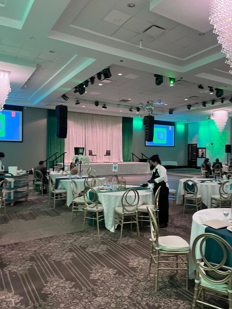 Close-up of ceiling-mounted line array speaker rental and stage lighting rig at a TD Bank corporate gala with a presenter at the podium