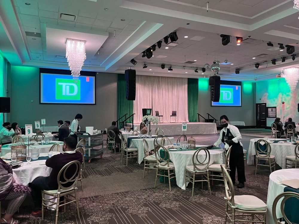 Grand ballroom corporate banquet with dual projection screens showing TD Bank logo, green wash lighting on walls