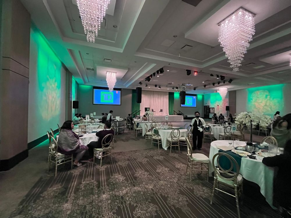 Bank corporate gala venue with two large projection screens, green uplighting, draped stage, and professional line array PA system rental