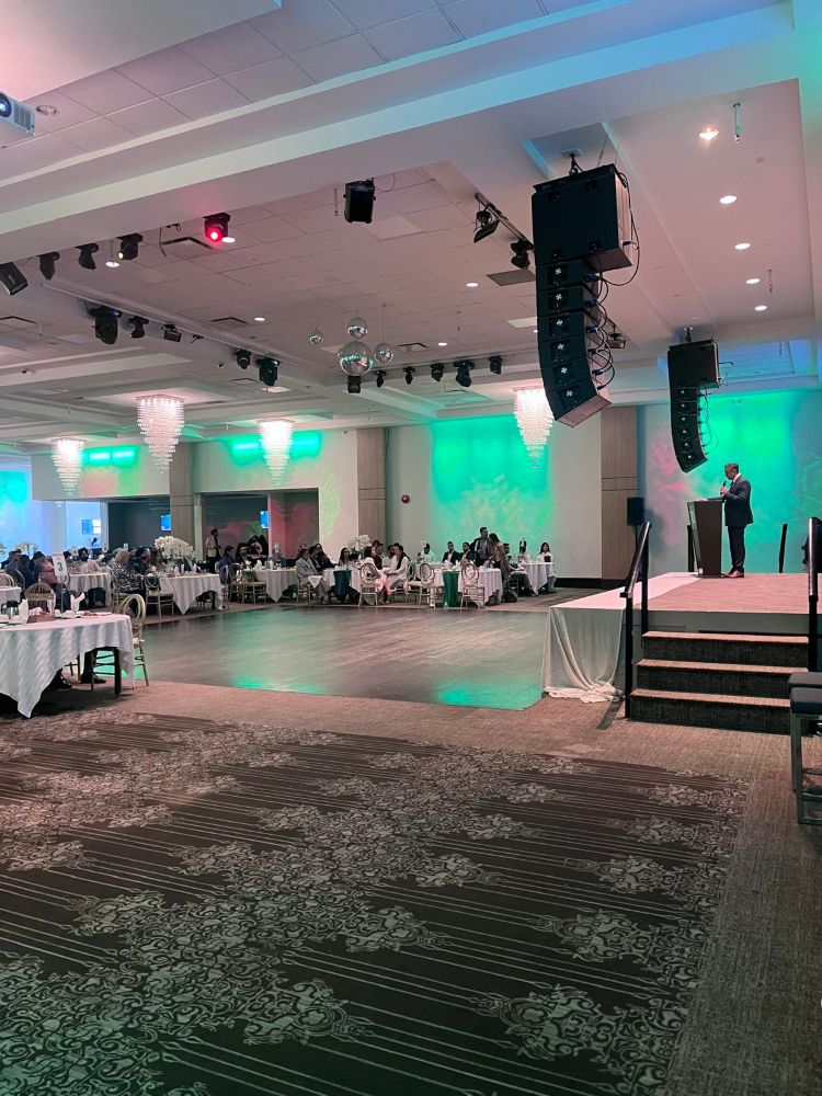 Wide ballroom view of a TD Bank event with dual screen rentals, professional stage lighting rig, crystal chandeliers, and line array speaker system