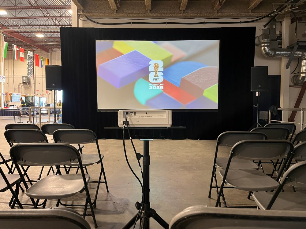 Projector rental on a tripod stand displaying the FIFA World Cup 2026 logo on a large fast-fold screen with black drape at a Maple Ridge watch party