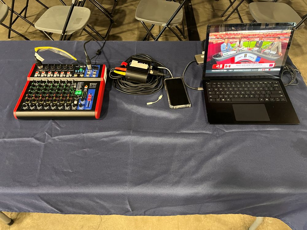 Close-up of a FIFA watch party streaming table setup with audio mixer, signal converter, and laptop broadcasting live World Cup coverage