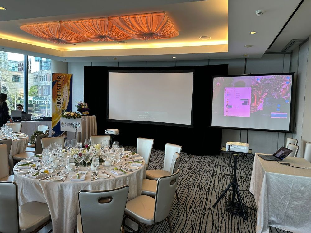 Short-throw projector rental projecting onto dual tripod screens in a luxury Fairmont Pacific Rim event room with fine dining table settings