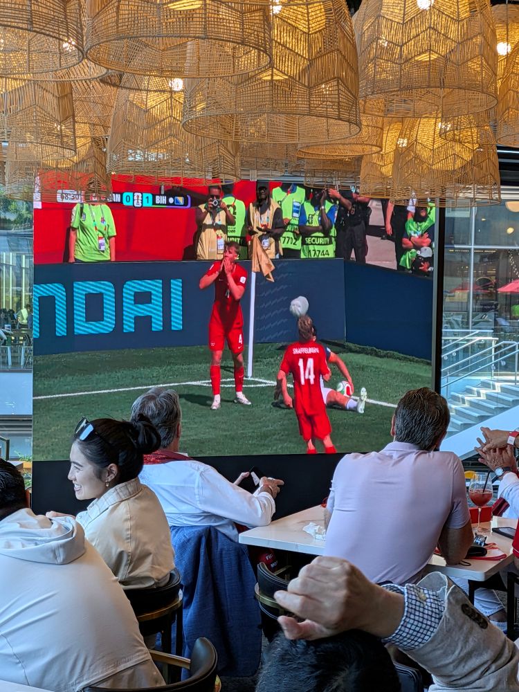 Large outdoor LED screen rental set up on a restaurant patio for a FIFA World Cup watch party with string lights and a PA speaker