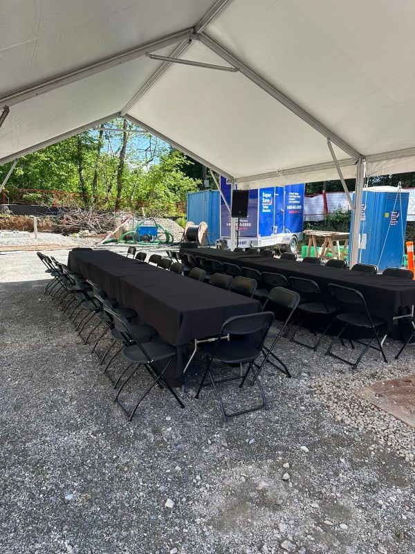 Rows of black-clothed tables and folding chairs set up under an event tent at an active construction site in Mission, BC